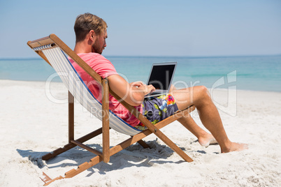 Full length of man using laptop at beach