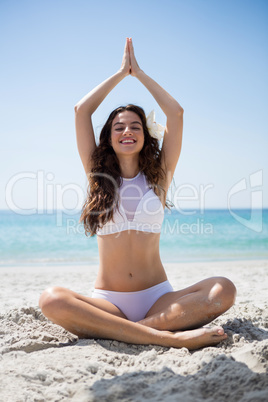 Smiling woman meditating while sitting on sand