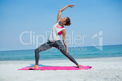 Full length of young woman exercising on mat at beach