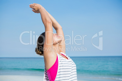 Young woman practicing yoga with arms raised at beach