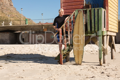 Man with surfboard standing on steps on beach hut