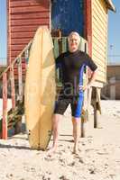 Portrait of man with surfboard standing against hut