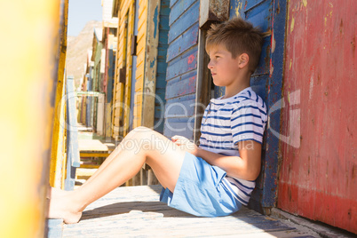 Boy looking away while sitting by beach hut
