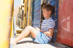 Boy looking away while sitting by beach hut