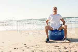 Portrait of smiling senior man sitting on ball against sea