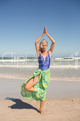 Senior woman practising yoga while standing against sea