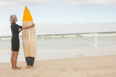 Rear view of senior woman holding surfboard while standing on shore