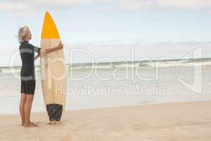 Rear view of senior woman holding surfboard while standing on shore