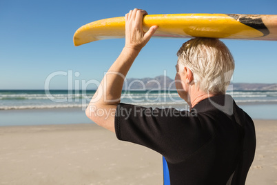 Senior man carrying surfboard on head at beach