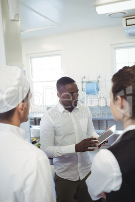 Male restaurant manager using digital tablet while briefing to his kitchen staff