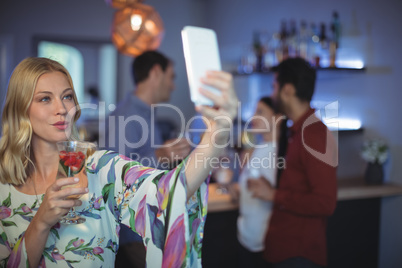 Beautiful woman holding glass of drink while taking a selfie