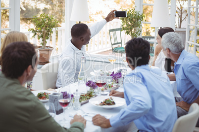 Group of friends taking selfie on mobile phone during lunch