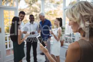 Woman using mobile phone while friends interacting in background