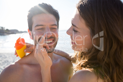 Happy young woman applying sunscream on man nose at beach