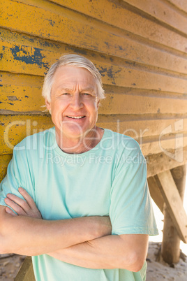 Senior man with arms crossed standing by beach hut