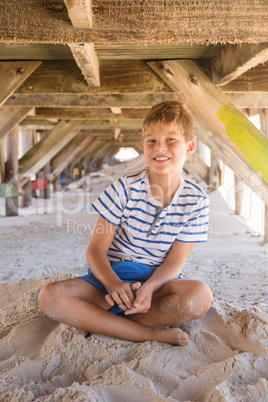 Portrait of boy playing with sand while sitting under hut