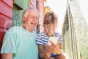 Happy boy with grandfather using smart phone while sitting by wall