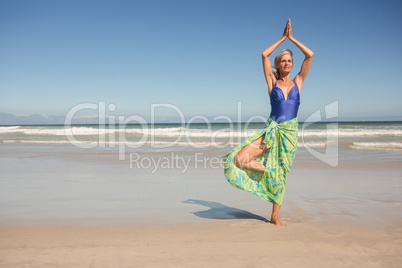 Senior woman practising yoga while standing against clear sky