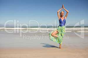 Senior woman practising yoga while standing against clear sky