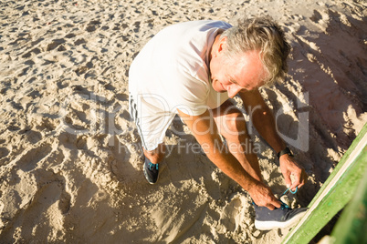 High angle view of man tying shoelace while standing on sand