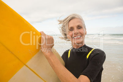 Close up of smiling senior woman holding surfboard while standing on shore