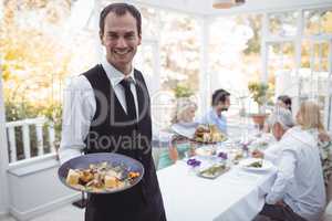 Portrait of smiling waiter holding food tray