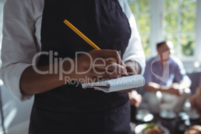 Waitress writing on notepad while friends interacting in background