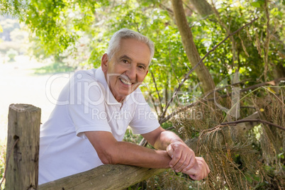Portrait of smiling senior man leaning on wooden fence