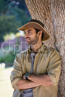Smiling man standing with arms crossed near tree trunk