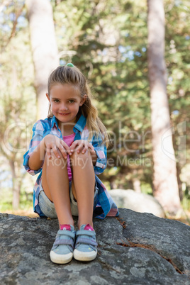 Smiling girl sitting on the rock in the forest