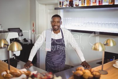 Portrait of smiling waiter standing counter