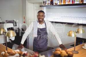 Portrait of smiling waiter standing counter