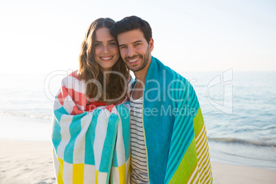 Portrait of happy young couple wrapped in blanket at beach