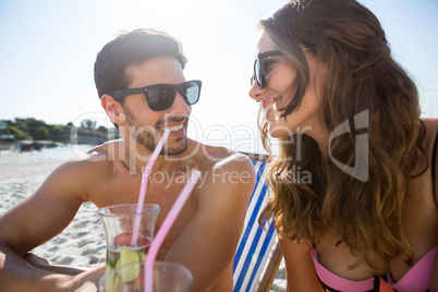 Smiling couple looking at each other while holding drinks at beach