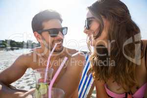 Smiling couple looking at each other while holding drinks at beach