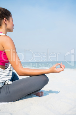 Full length of young woman meditating on sand at beach