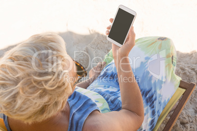 Senior woman using smart phone while sitting on chair at beach