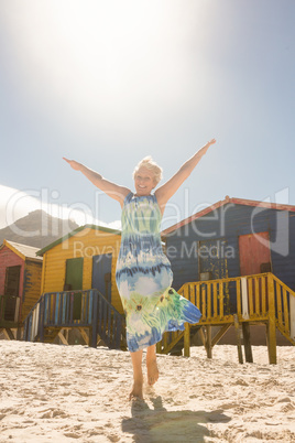 Portrait of smiling senior woman with arms raised walking on sand at beach