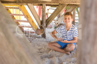 Portrait of smiling boy playing with sand while sitting under hut