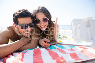 Happy couple taking selfie while lying together on blanket at beach