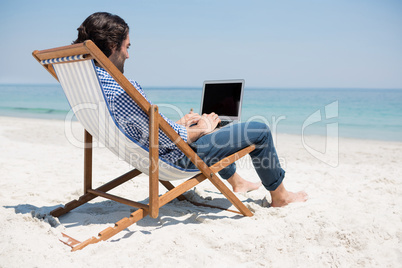 Side view of man using laptop at beach