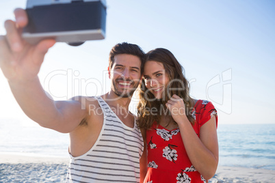 Happy young couple photographing through camera at beach