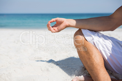 Low section of man meditating at beach