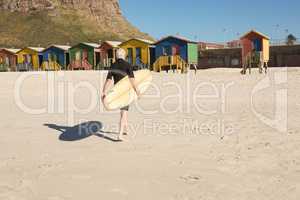 Man with surfboard walking on sand against beach huts