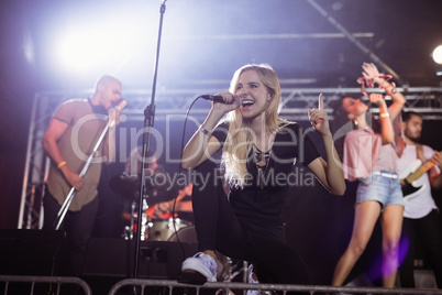 Young female singer performing with musicians at nightclub during music festival