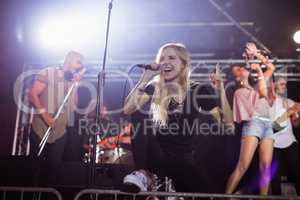 Young female singer performing with musicians at nightclub during music festival