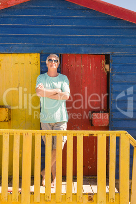 Senior man with arms crossed standing by railing of beach hut