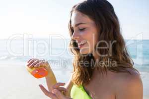 Smiling young woman pouring sunscream on finger at beach