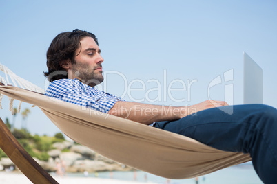 Side view of man using laptop while relaxing in hammock