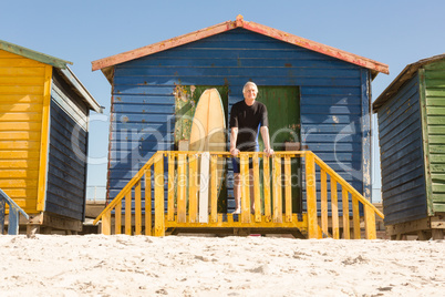 Portrait of man standing with surfboard at beach hut